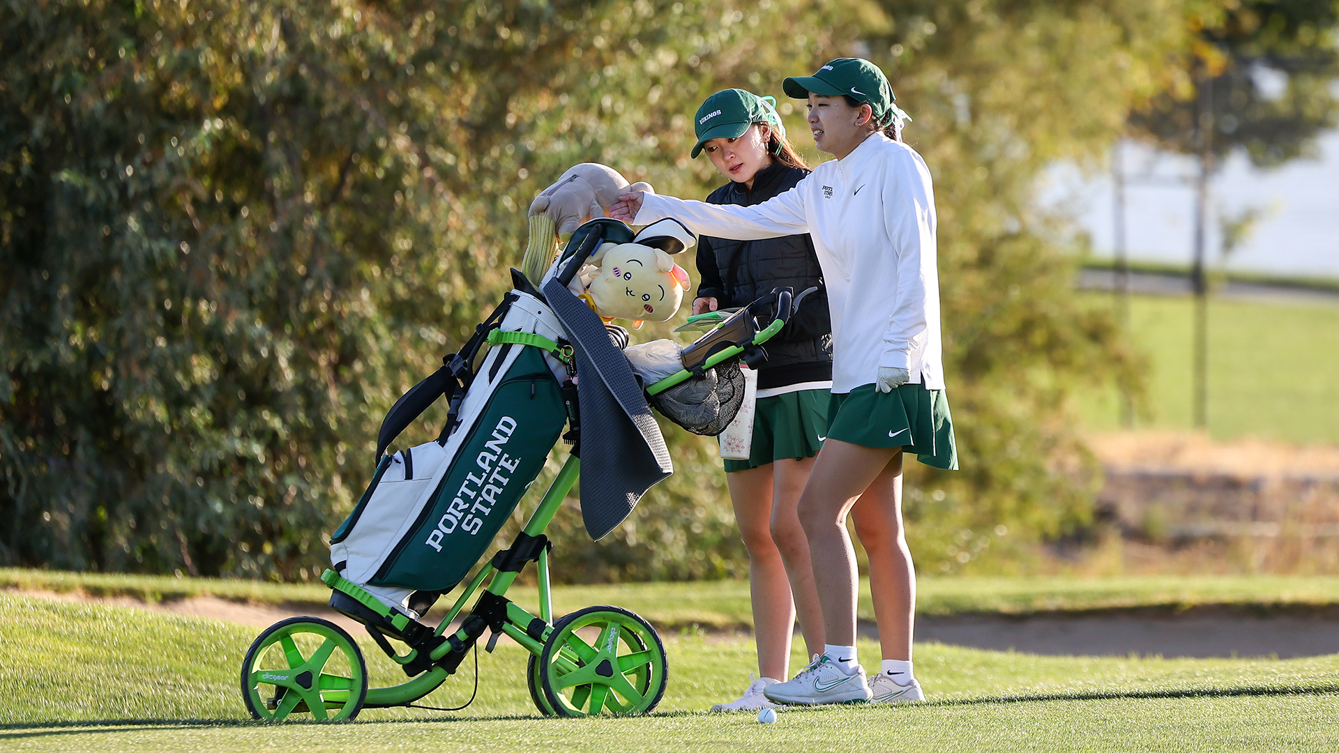 Portland State women's golfer Momo Udom selects a club after talking with assistant coach Payten Shimizu.