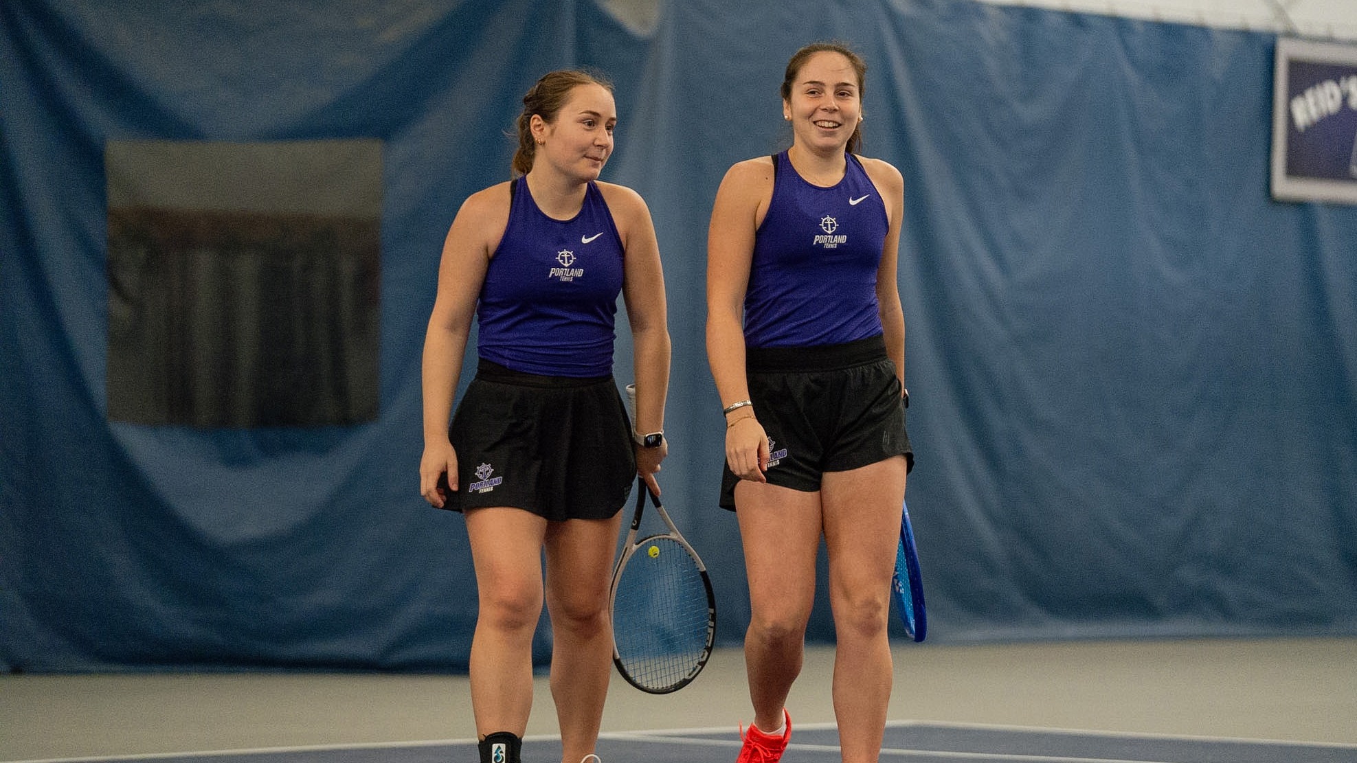 Alaia Rubio Perez and Maria Galatescu chat between doubles points during a home dual match.