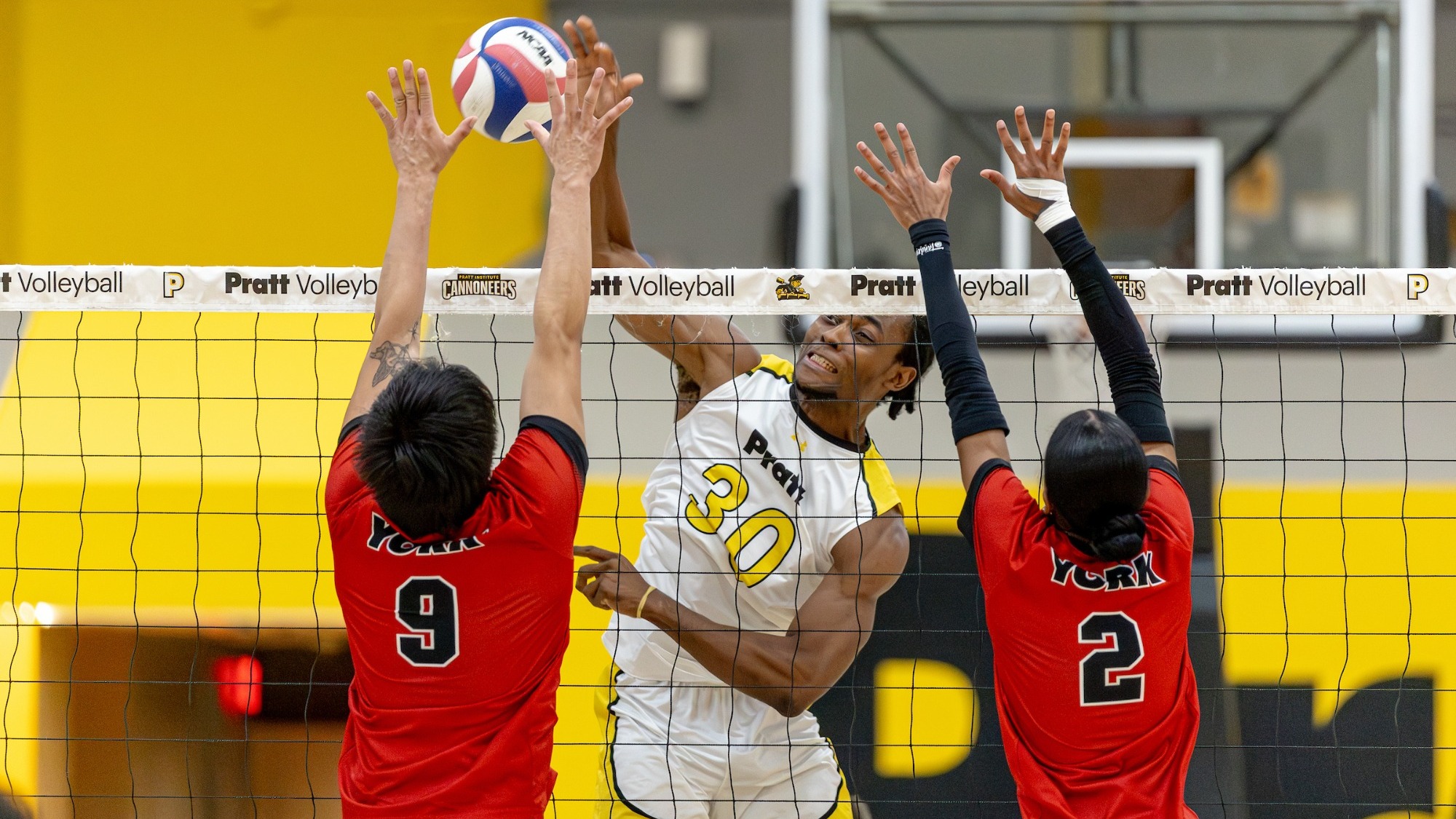 Morvens Regis spikes the ball with two blockers at the net.