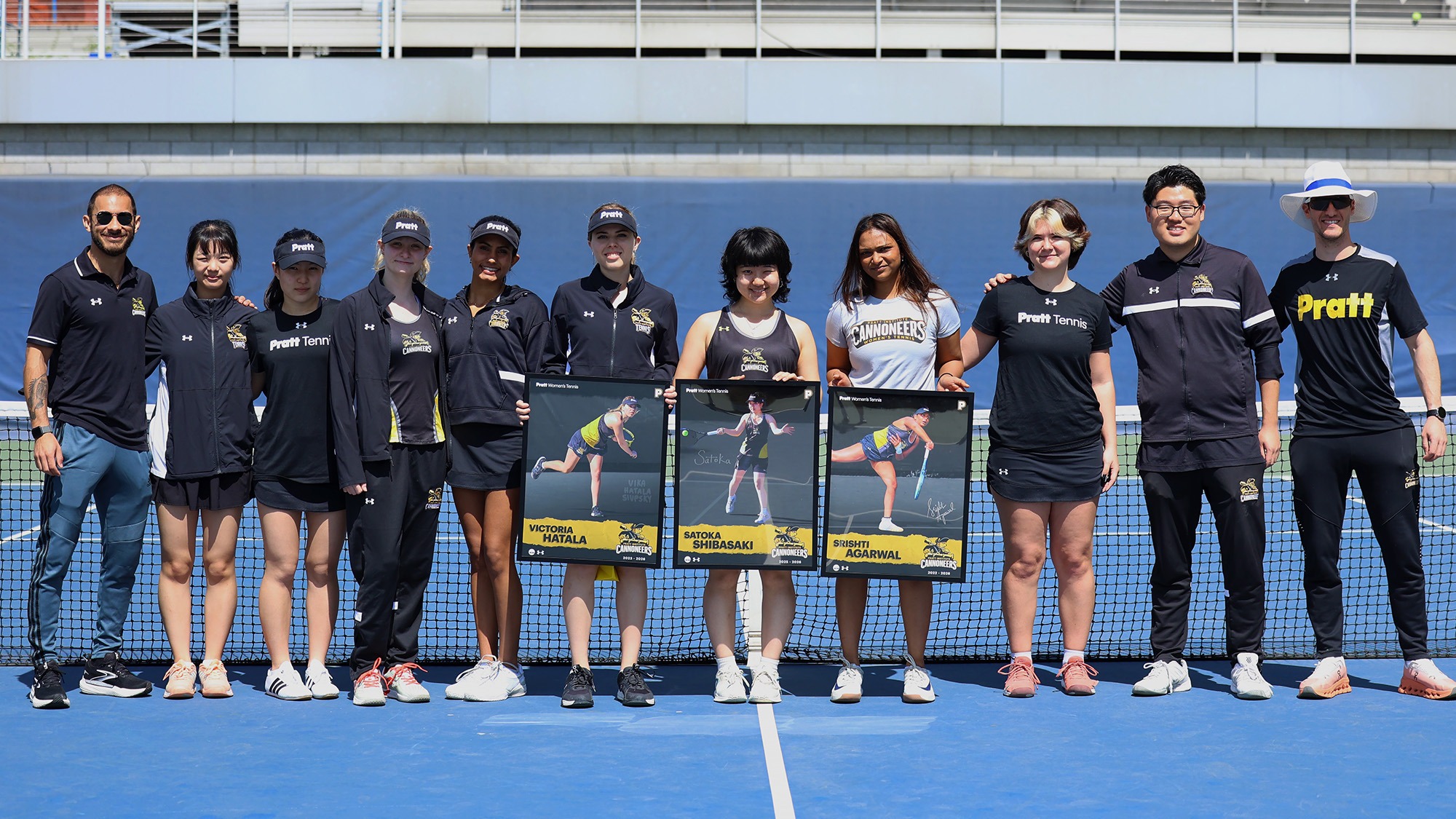 Women's Tennis poses on Senior Day at center court with their three seniors holding their senior posters.
