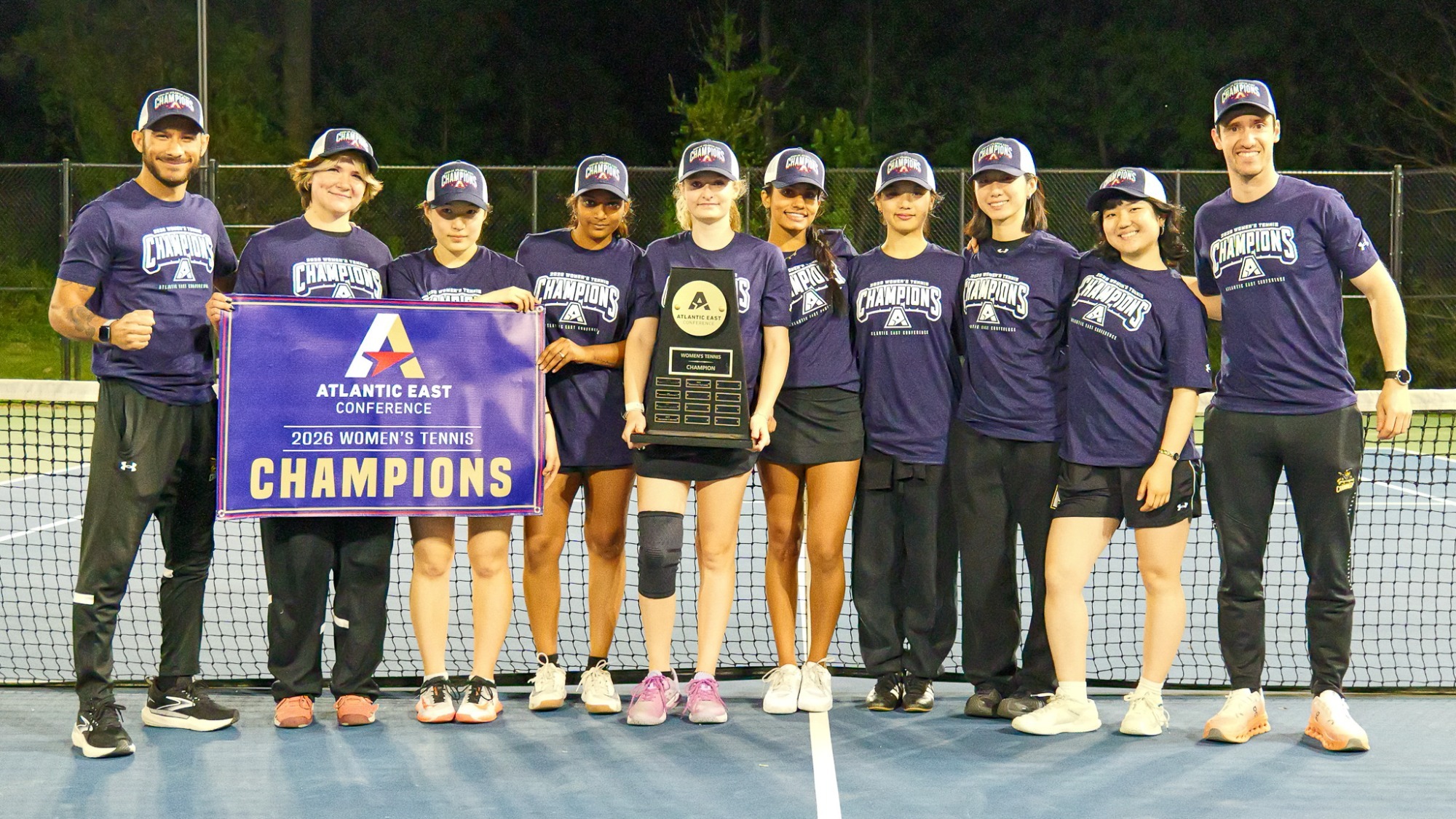 Women's Tennis poses with the 2026 Atlantic East Tournament Championship trophy and banner