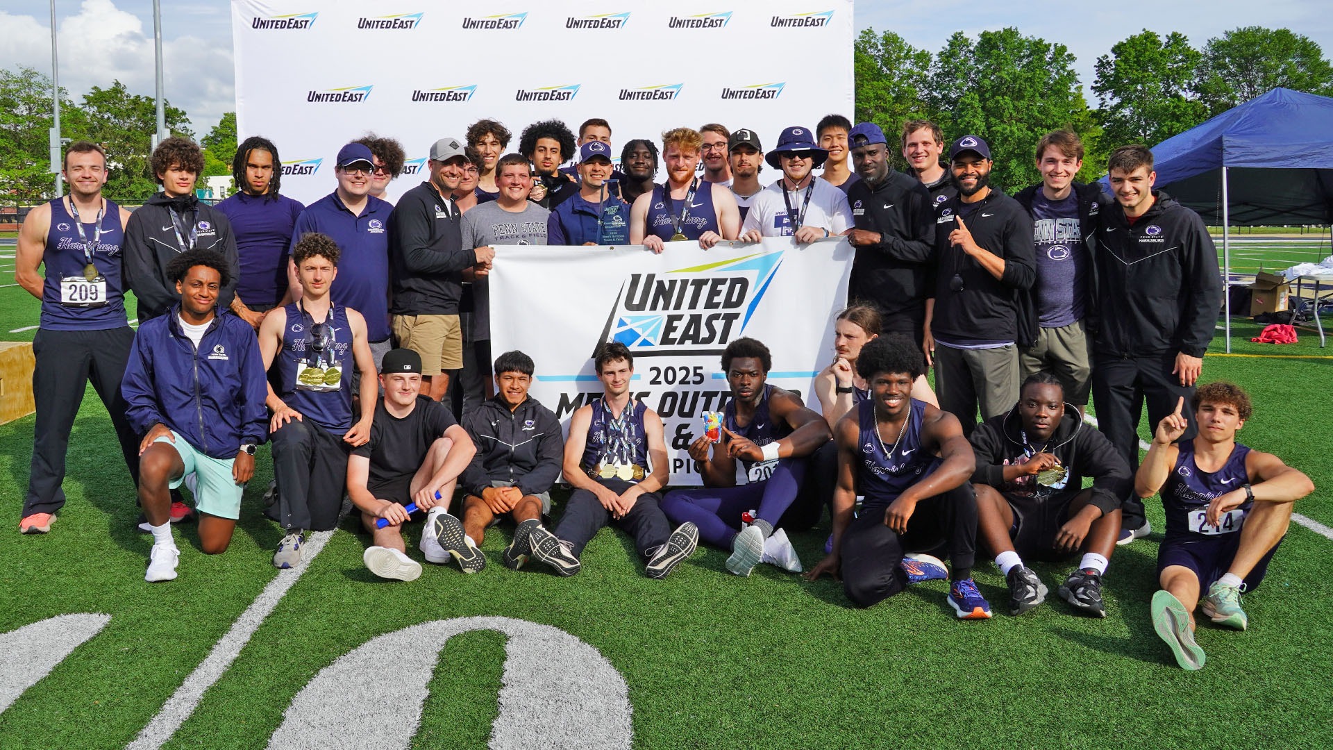 men's track & field poses with the united east championship banner and trophy after winning the conference title in 2025