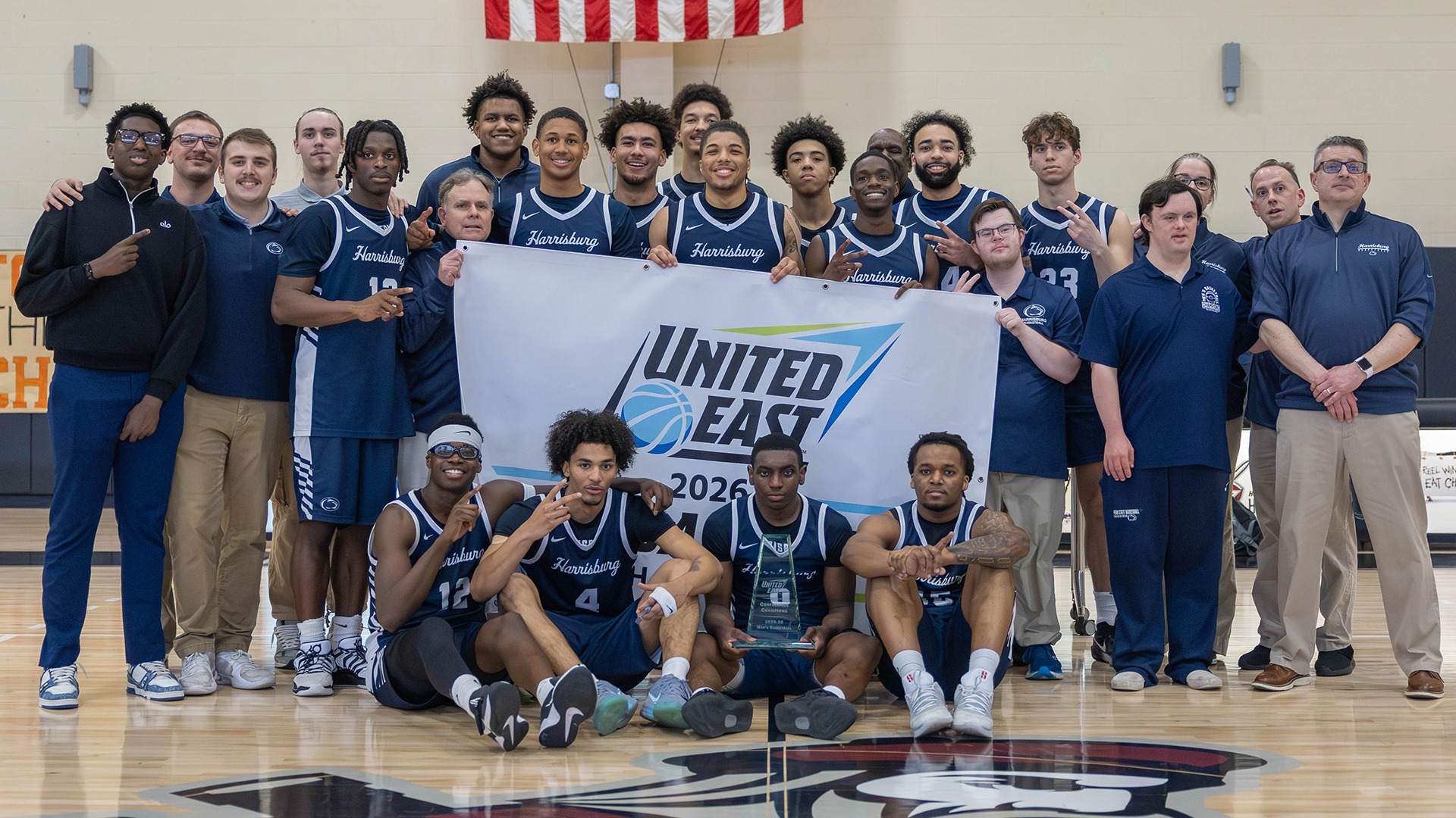 2025-26 mens basketball team poses with the united east championship banner