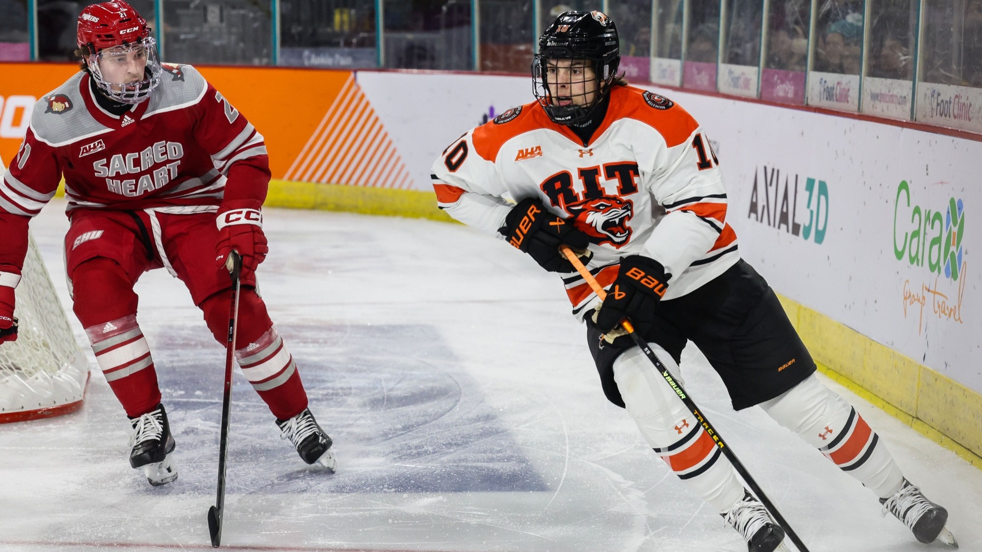 a men's hockey player skating along the boards around a defender