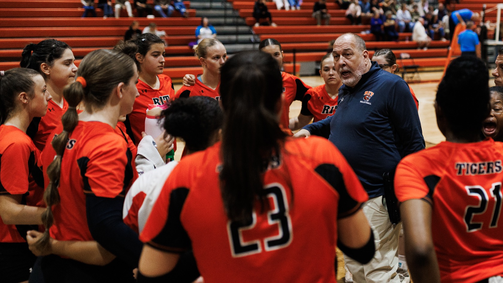 a women's volleyball team huddle with the coach talking in the middle