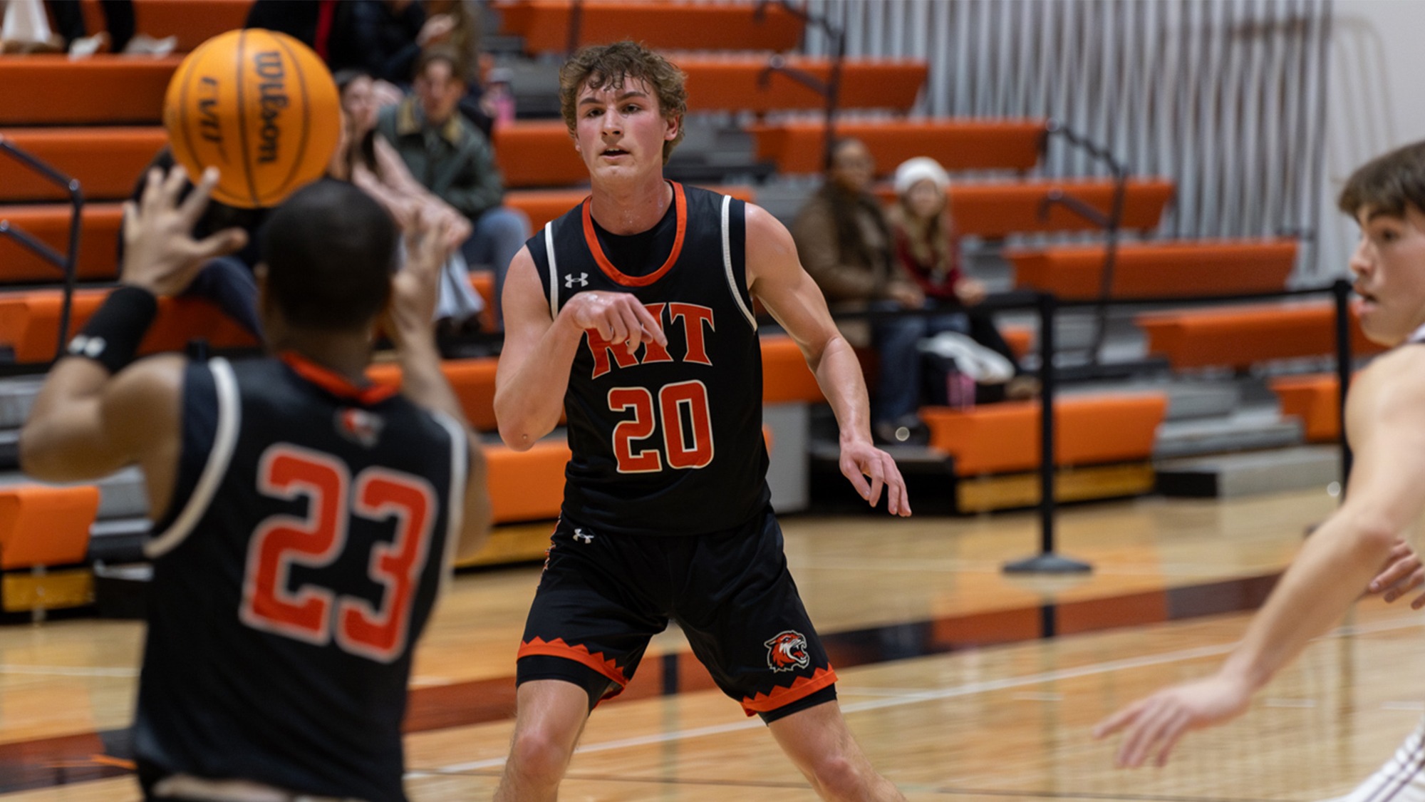 a men's basketball player for Rochester Institute of Technology make a pass to a teammate under the basket