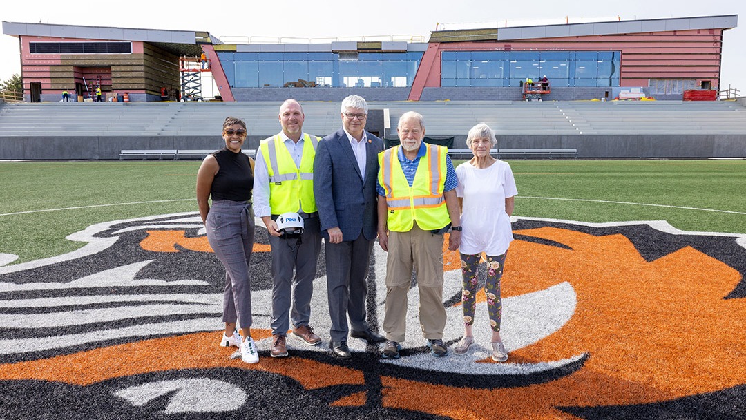 The Judson family stands at midfield with RIT leadership at the new Judson Stadium. From left: Jacqueline Nicholson, executive director of RIT Athletics; Rufus Judson, CEO of Pike Construction Services; RIT President Bill Sanders; former RIT Trustee Tom Judson; and Ebets Judson.