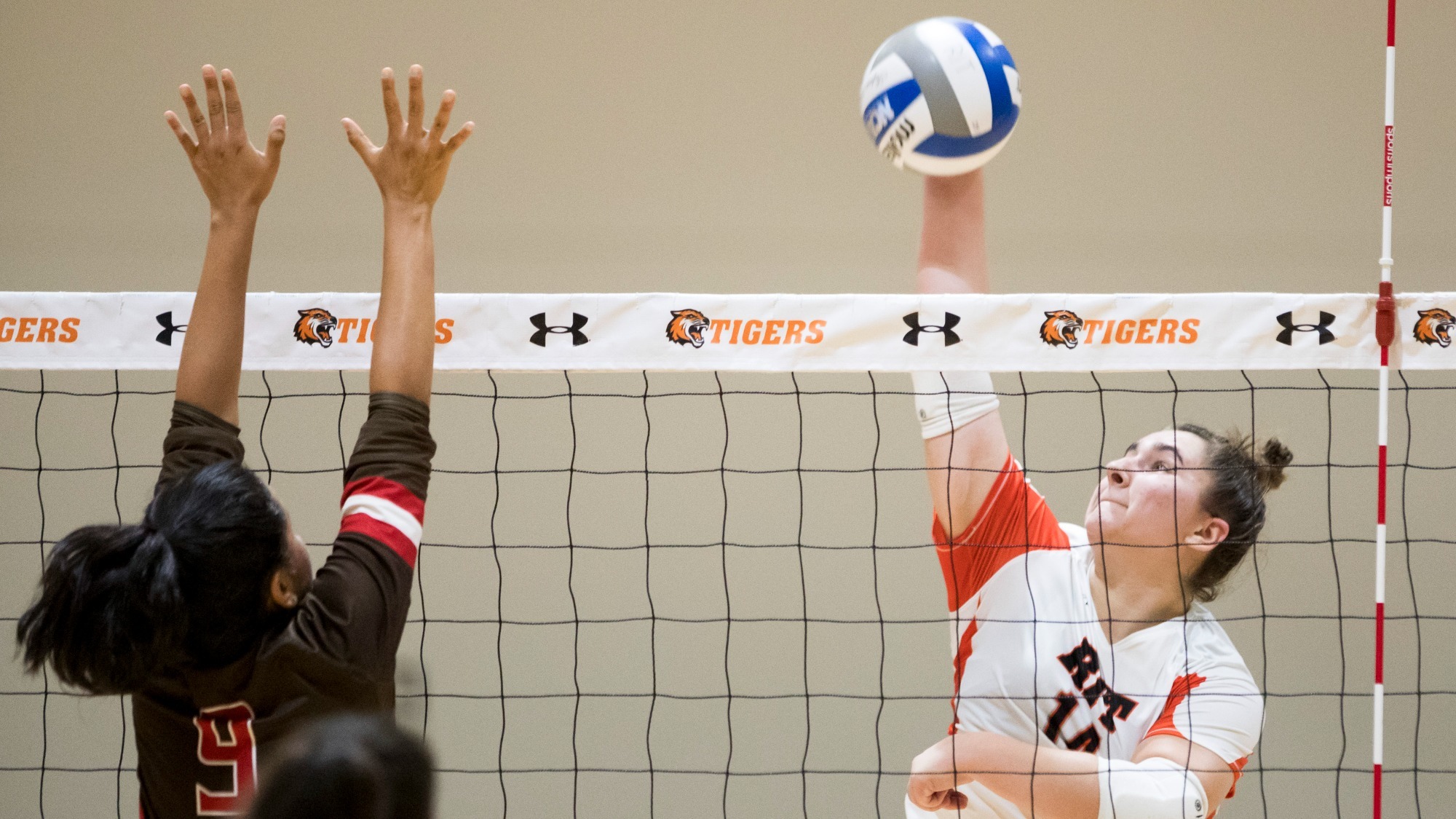 a women's volleyball player attacking at the net