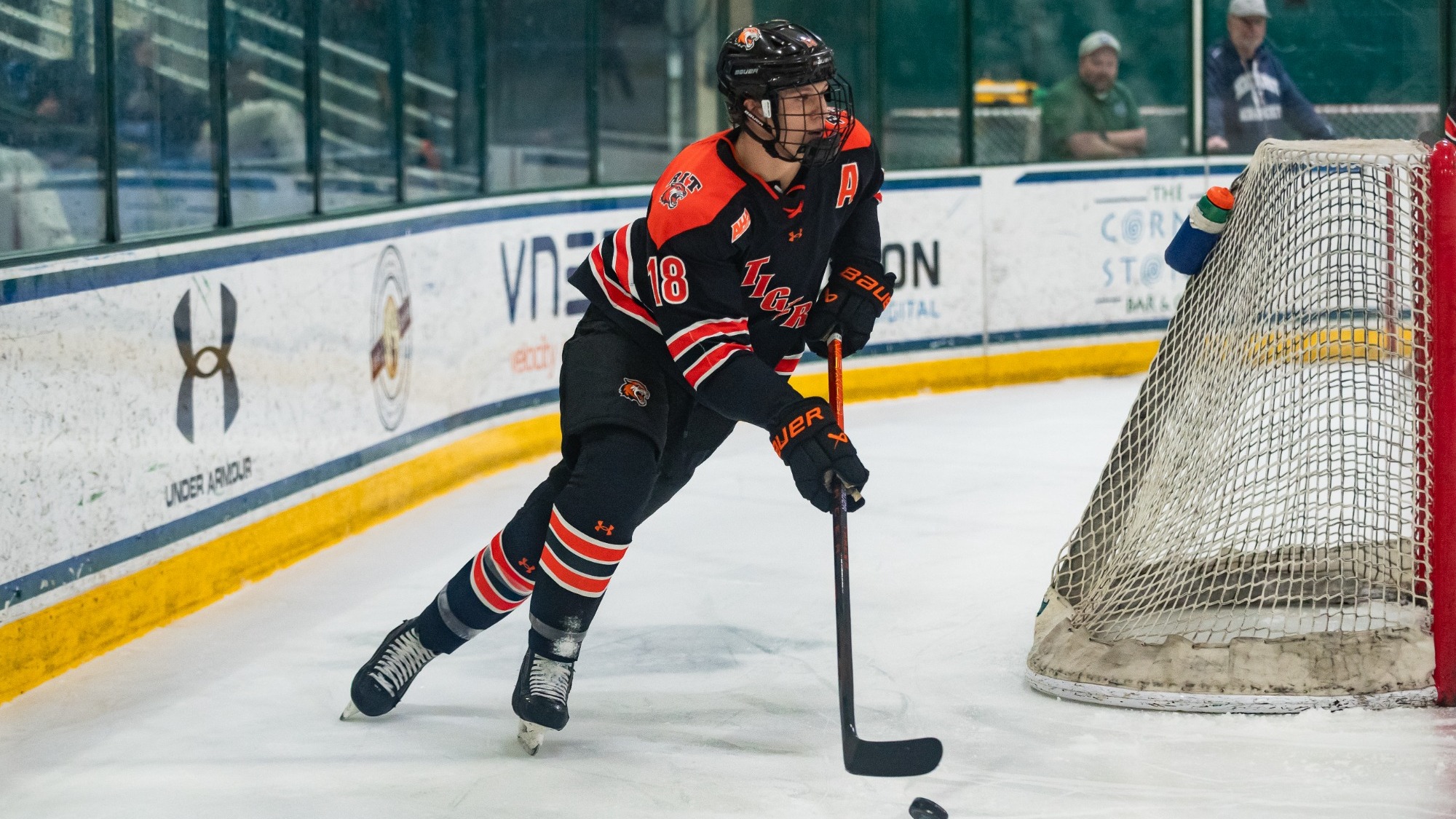 a men's hockey player skating behind the goal with a puck