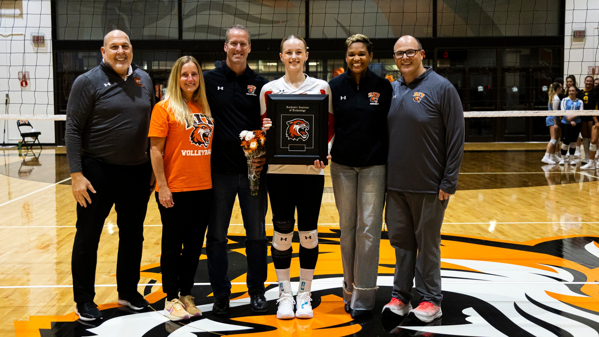 a women's volleyball player posing with her family and coach on senior night