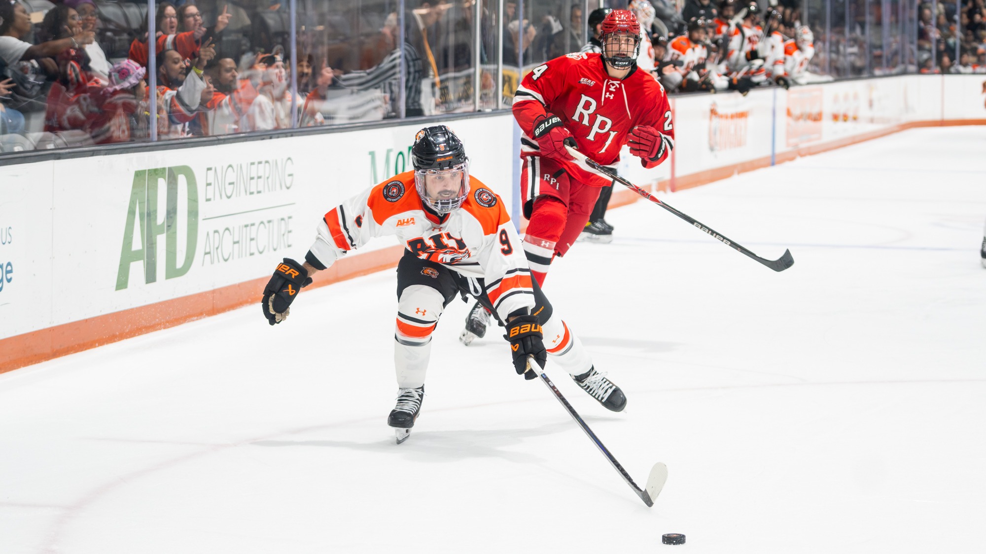 a men's hockey player stretches for a puck in front of an opponent