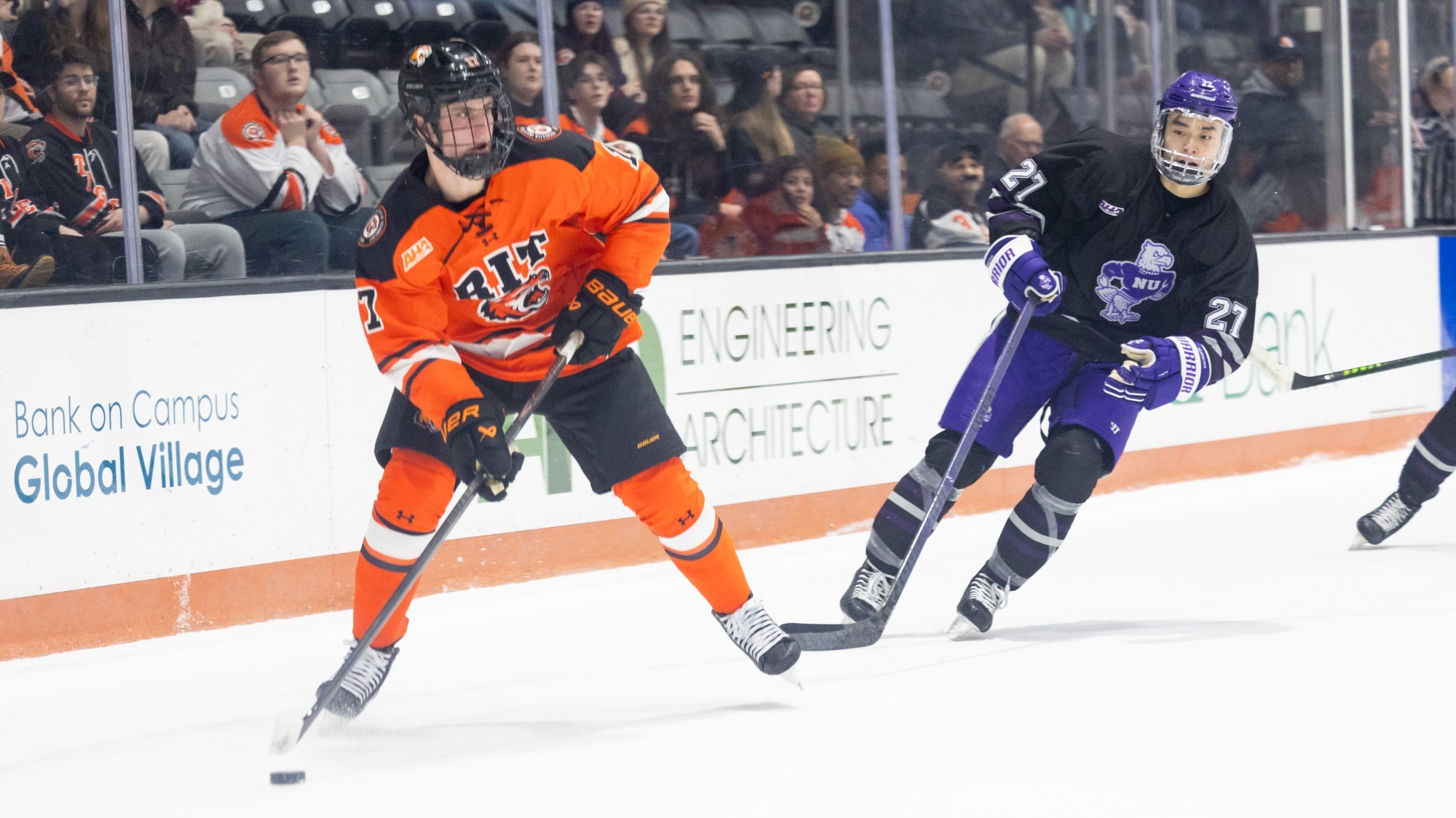 a men's hockey player looks to pass along the boards with a defender behind him.