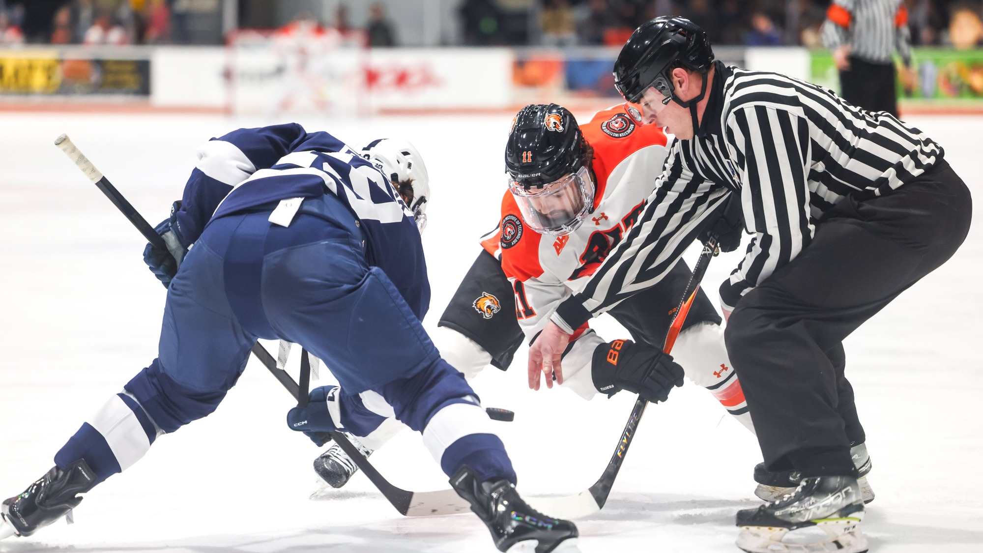 two men's hockey players take a faceoff in front of a referee