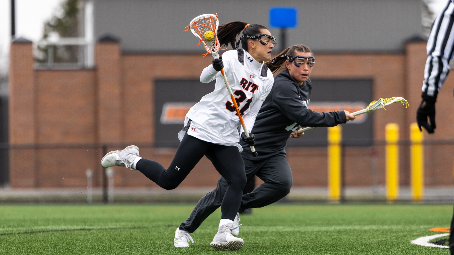 A women's lacrosse player cradles with the ball past a defender