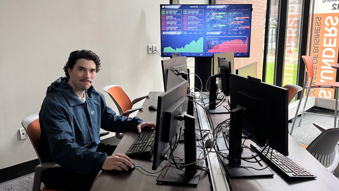 a student sitting in front of a large computer setup, including multiple screens