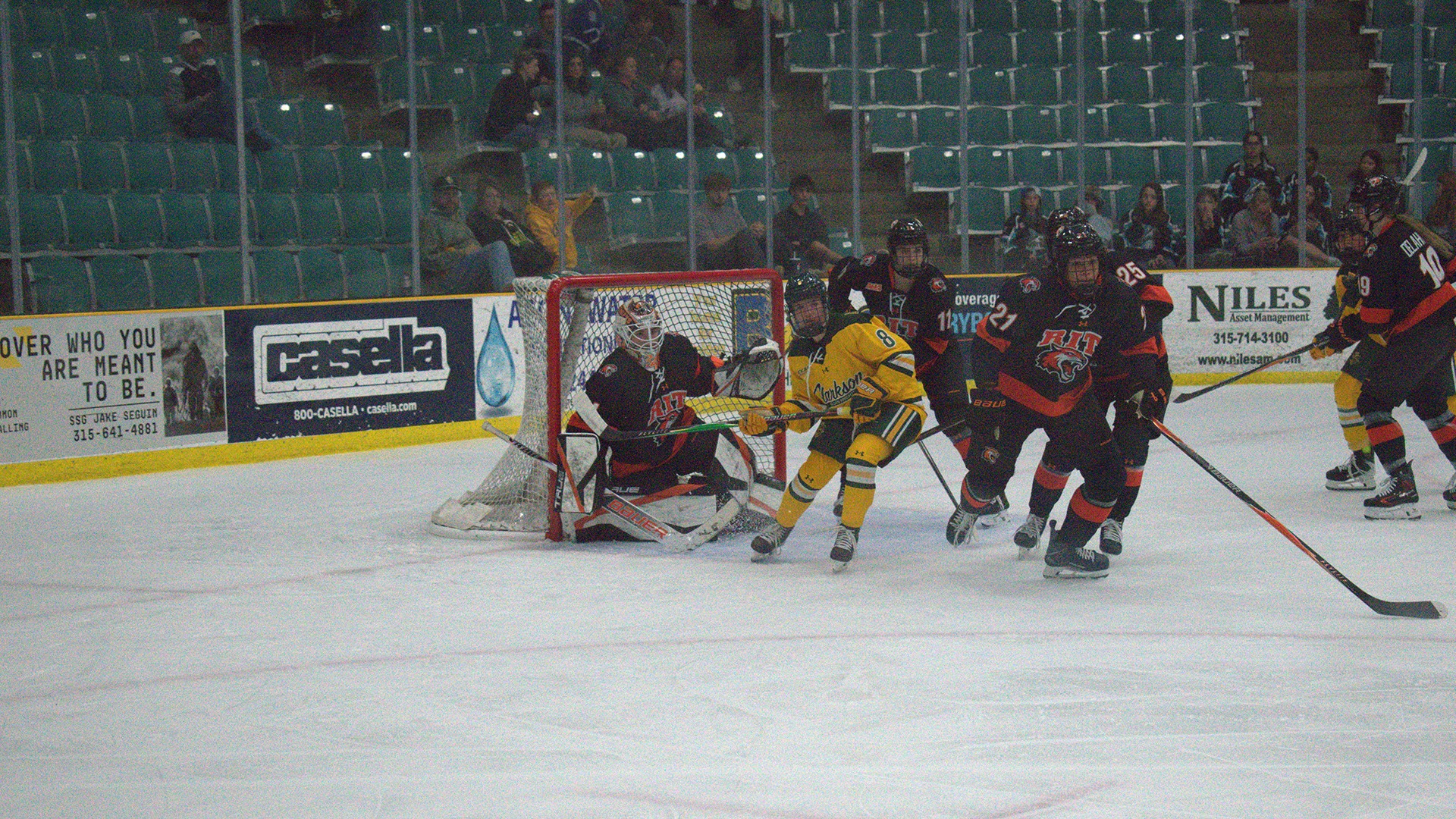 A photo of RIT women's hockey players scrambling to get a loose puck against Clarkson (Sept. 26)