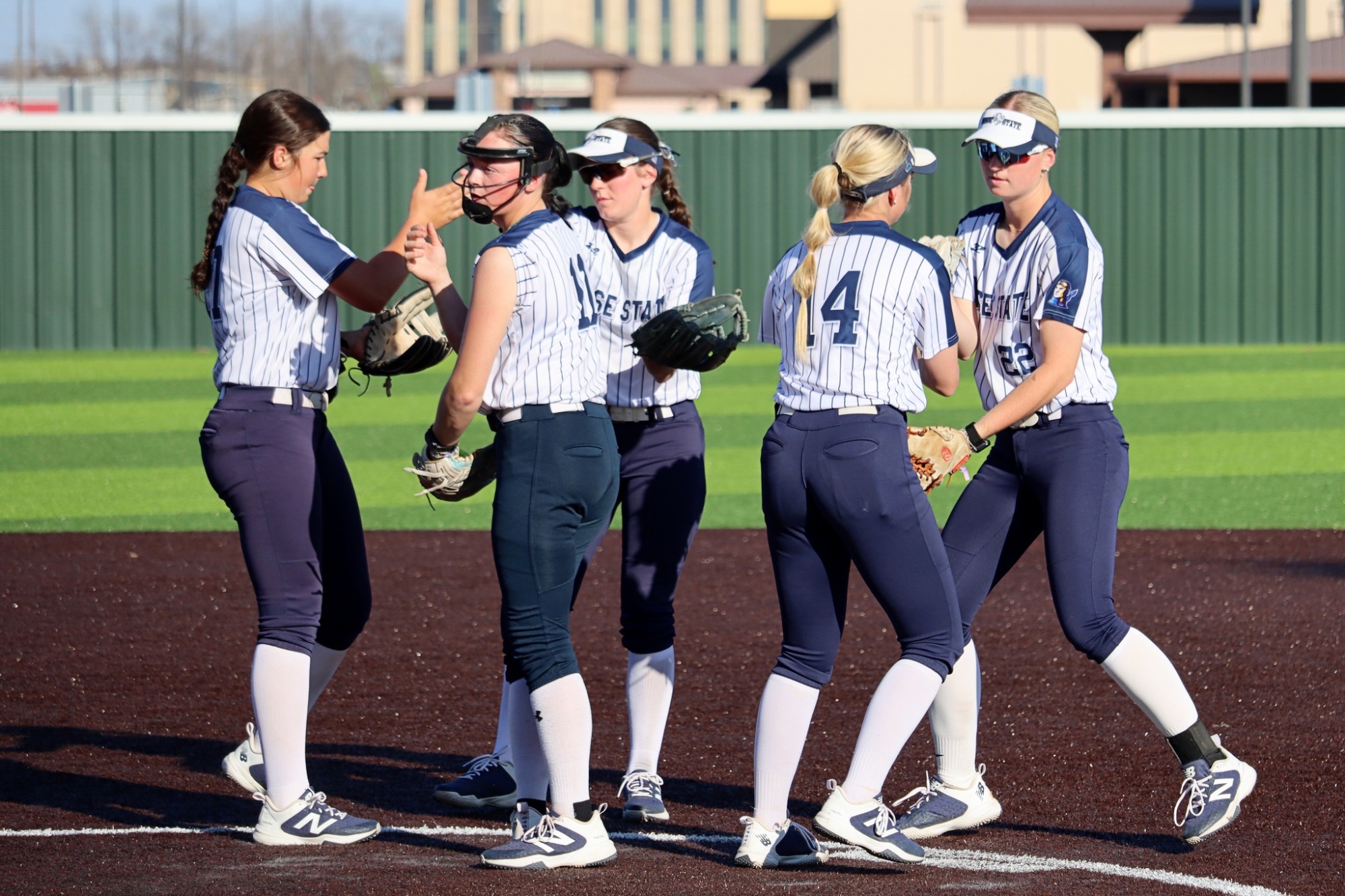 Rose State College softball infielders meeting at the mound hitting gloves