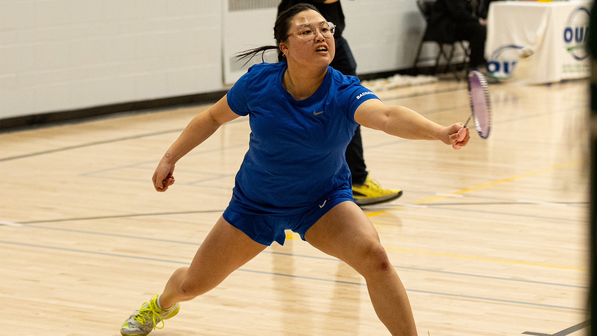A TMU badminton player reaches their racket forwards to hit the shuttlecock.