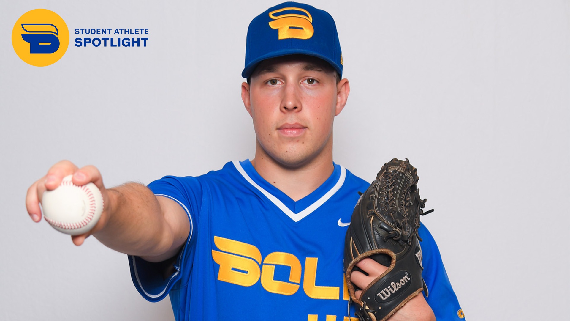 TMU baseball player poses against a white back drop with his arm outstretched holding a baseball.