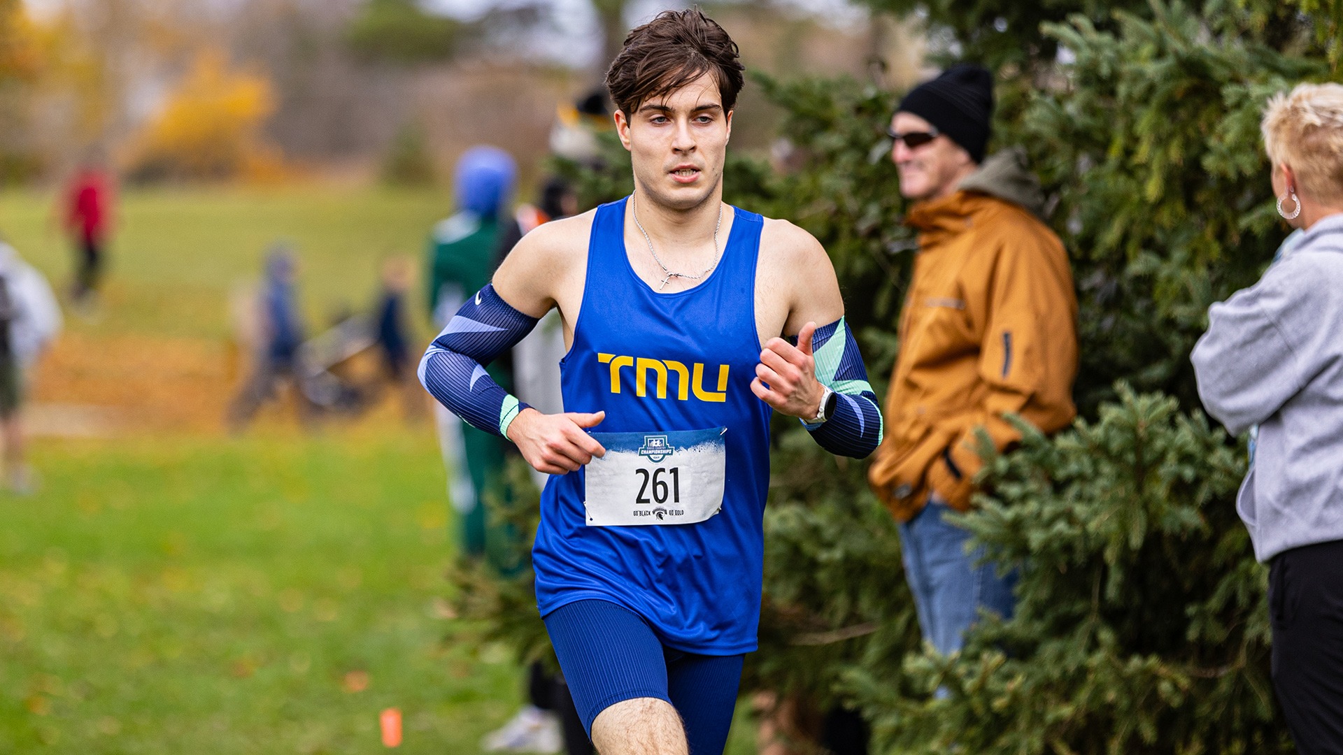 A TMU runner races along a tree-lined course with spectators