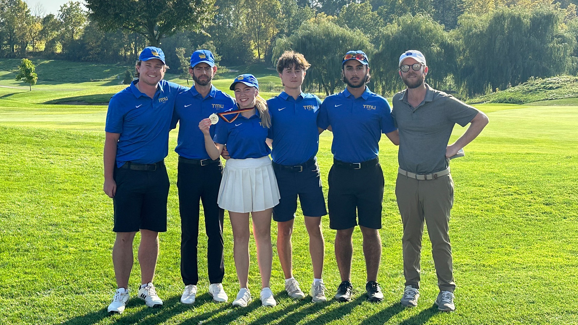 A TMU golfer holds up her gold medal, surrounded by her teammates.