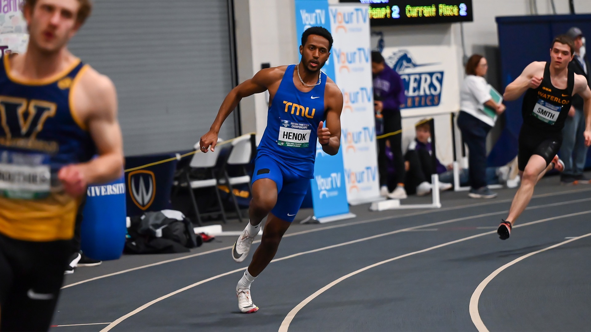 A TMU sprinter turns a corner on the track with opponents on both sides of him.