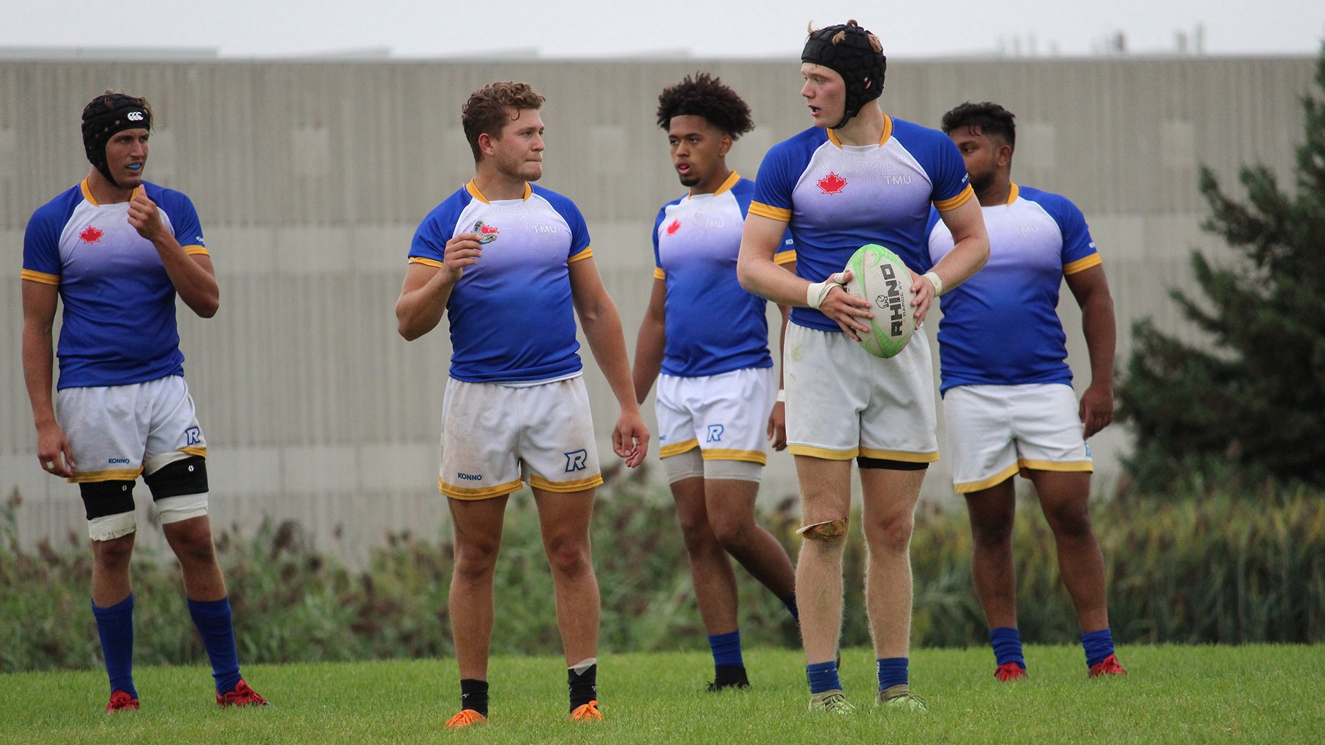 Five TMU rugby players stand waiting for play to resume.