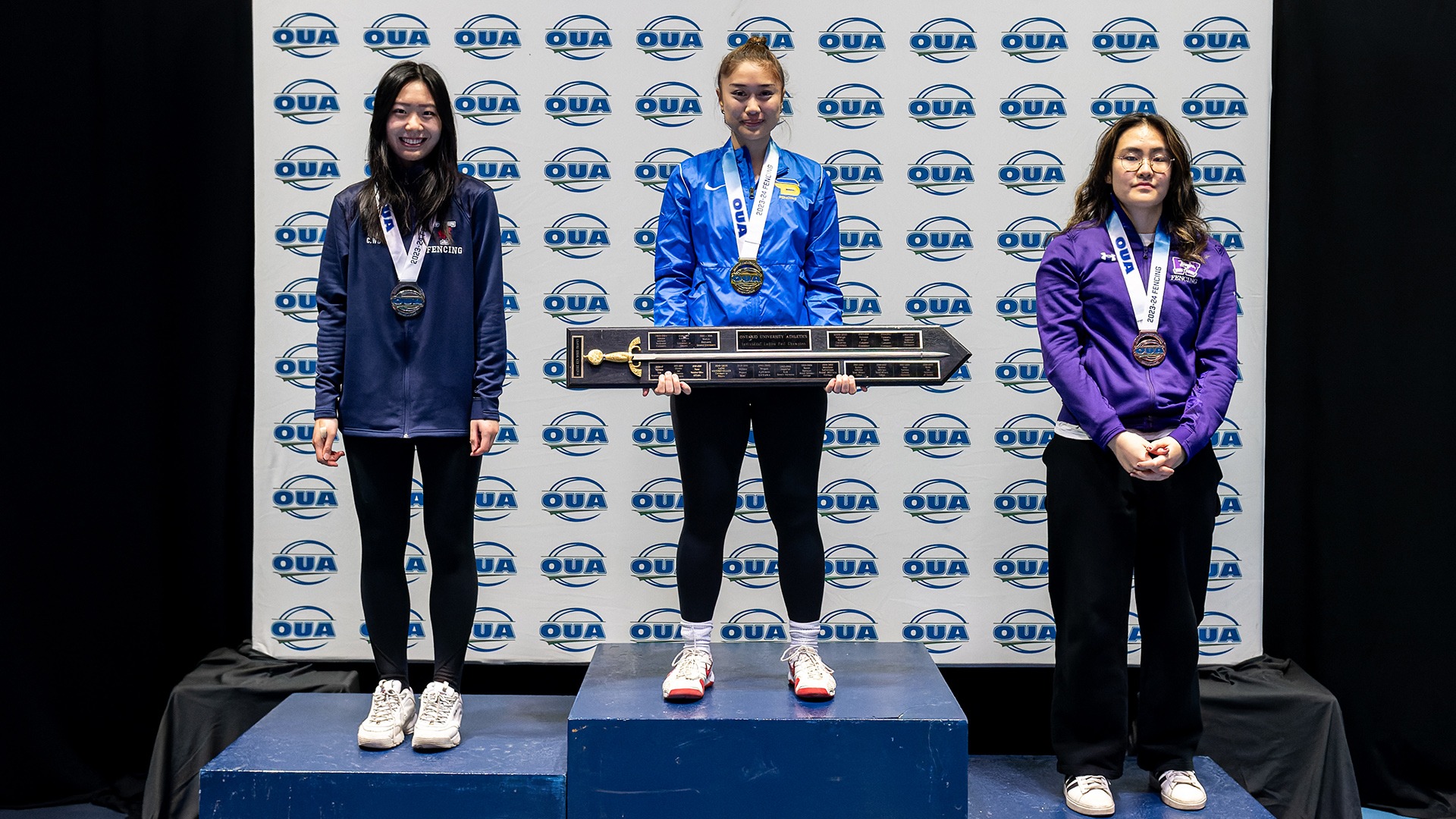 Three women stand on a podium wearing their championship medals