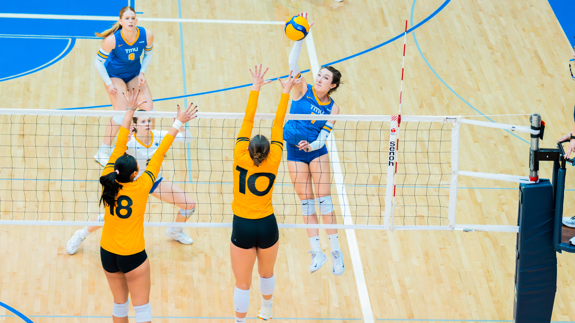 Bold Outside Hitter Hannah Bellai Leaps for an Attack Over Two Warriors Defenders