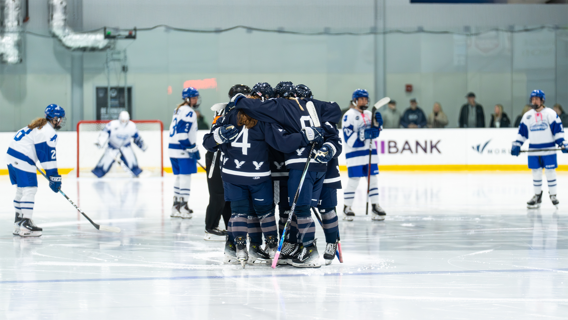 Women's ice hockey players huddle before faceoff at center ice