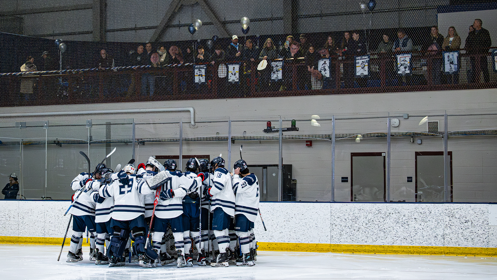 Men's ice hockey team huddles pregame while senior families look on
