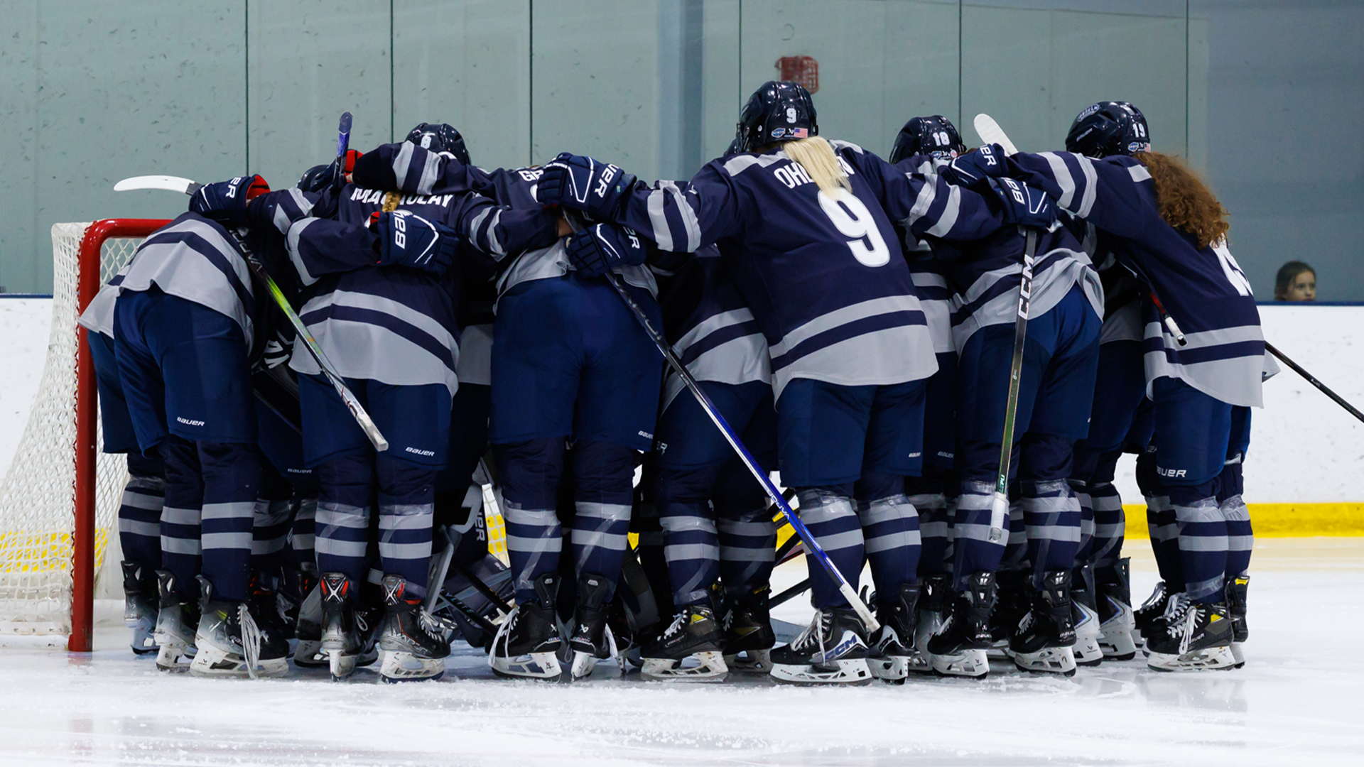 Women's ice hockey team huddles around goal