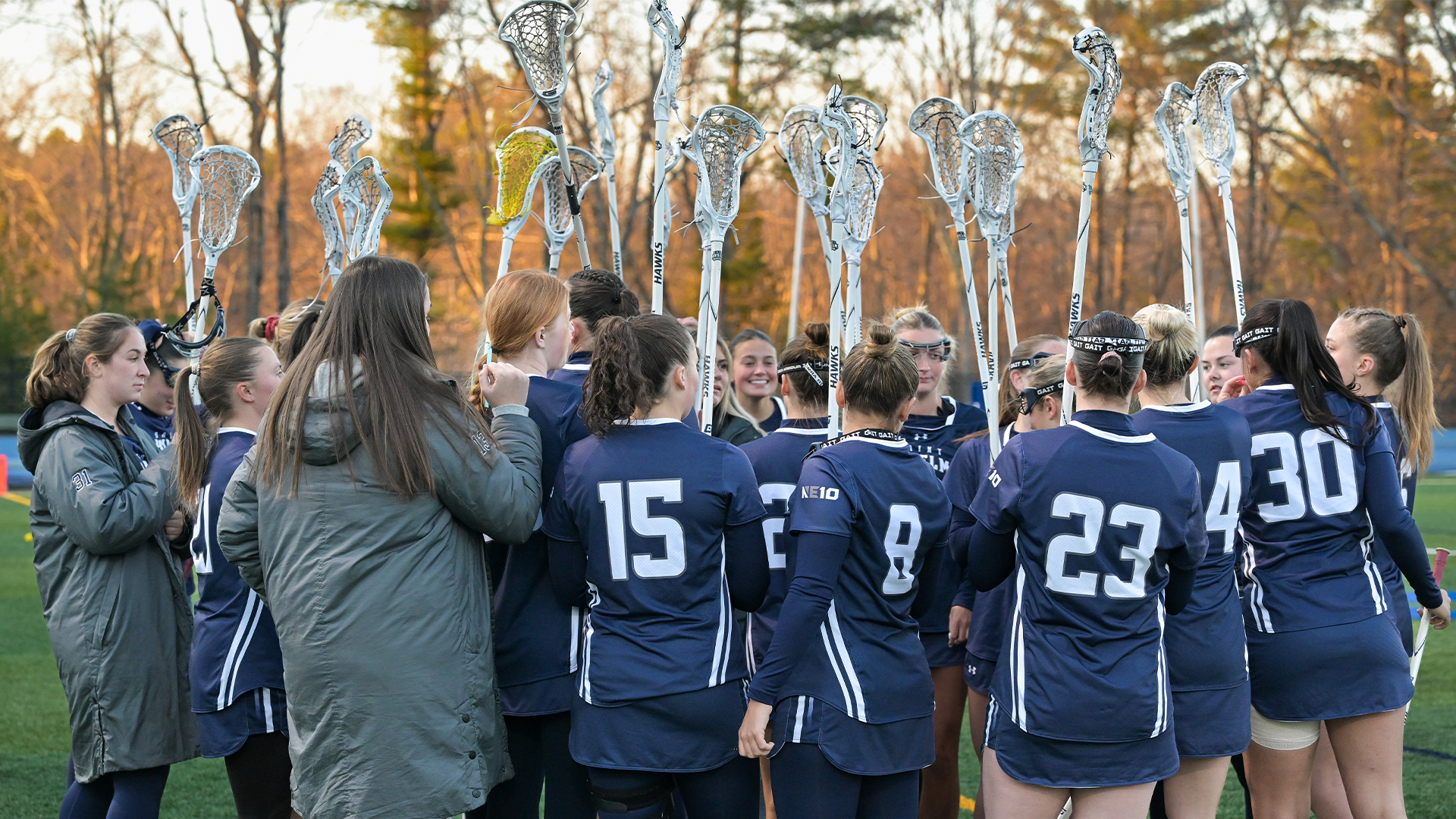 Women's lacrosse team huddles with sticks raised