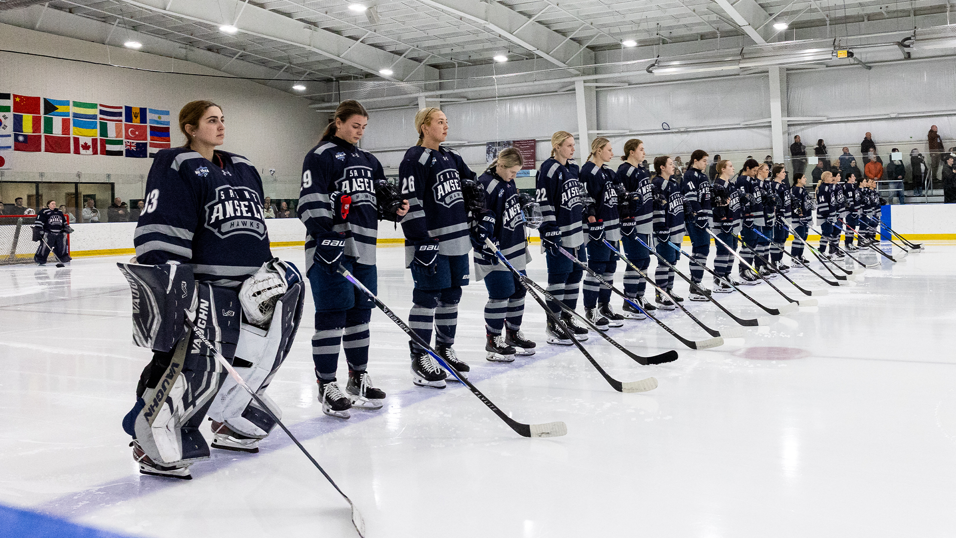 Women's ice hockey players stand on blue line for national anthem