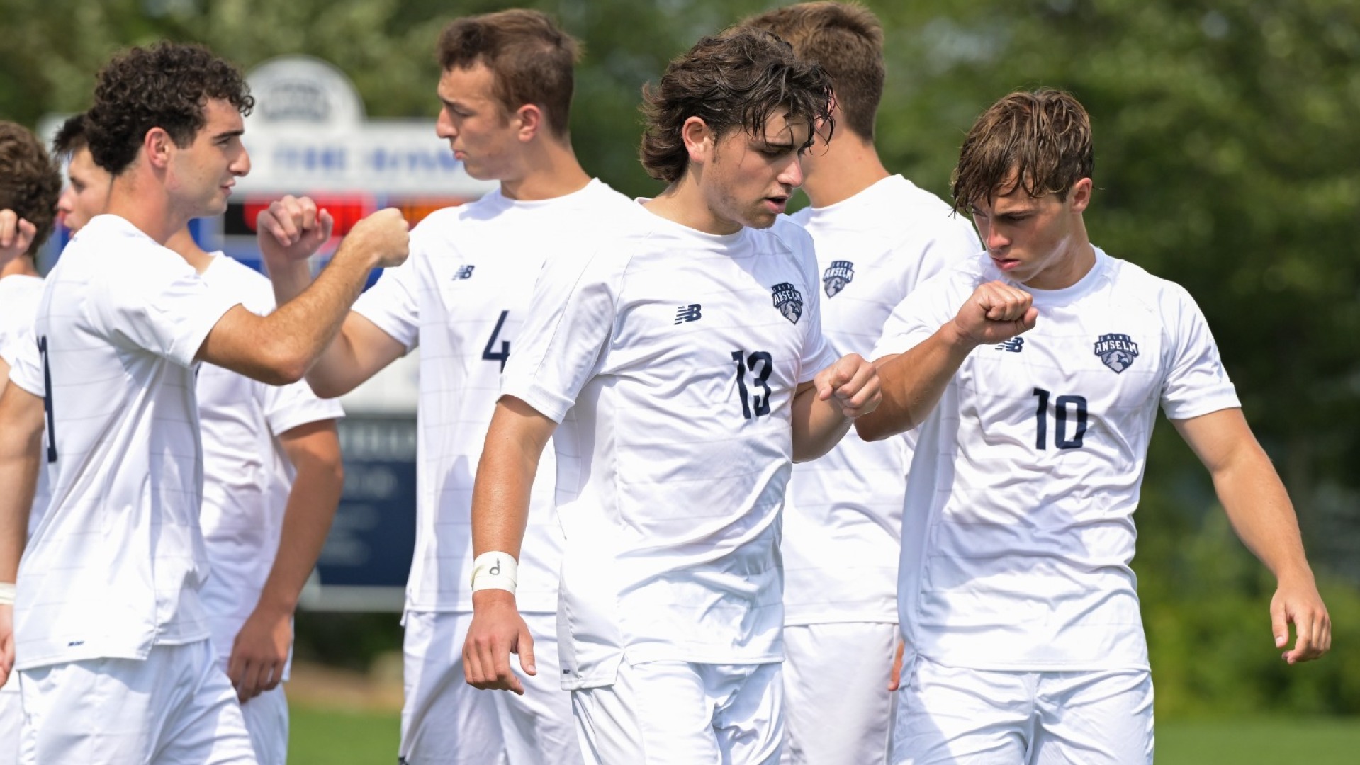 Saint Anselm men's soccer players exchange fist bumps on the field before a match. 