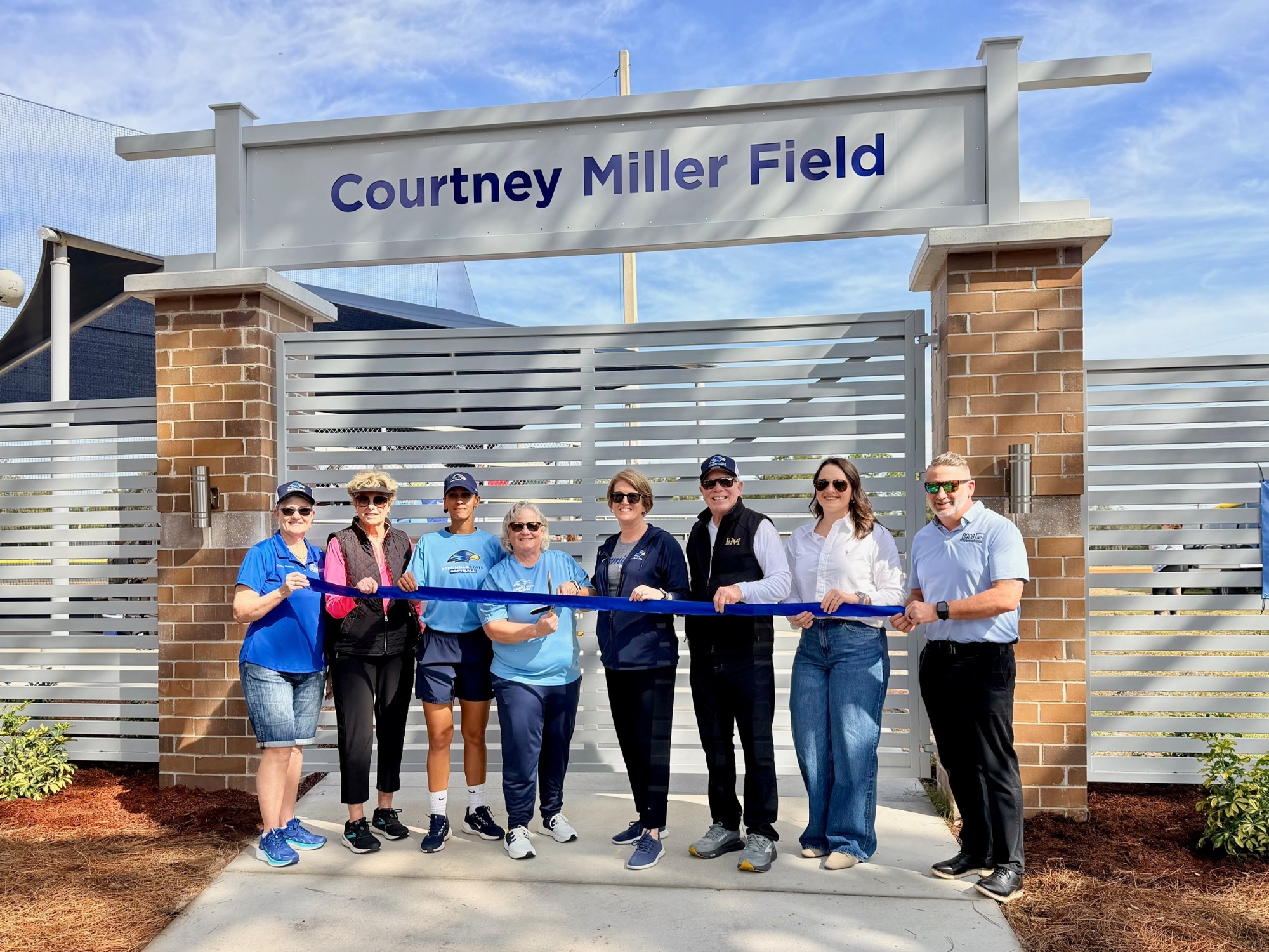 People standing in front of a fence holding a ribbon