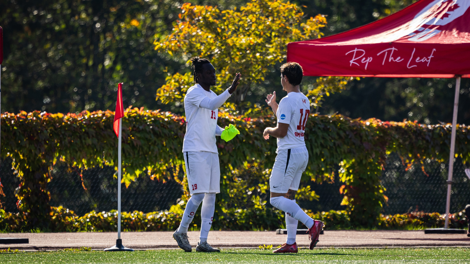 Two SFU Men's Soccer players high five on the field.