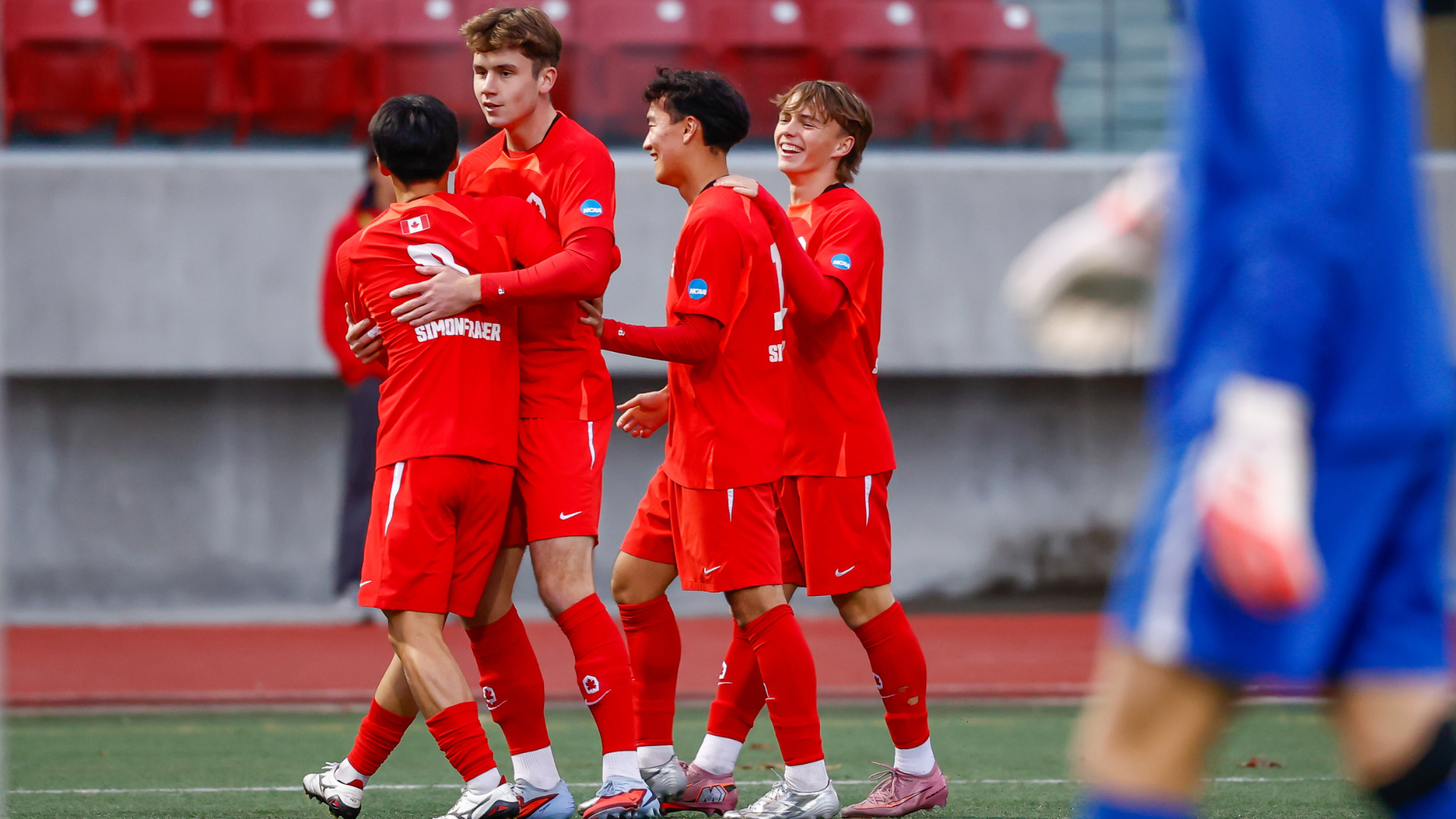 Four SFU Men's Soccer players celebrate on the pitch.