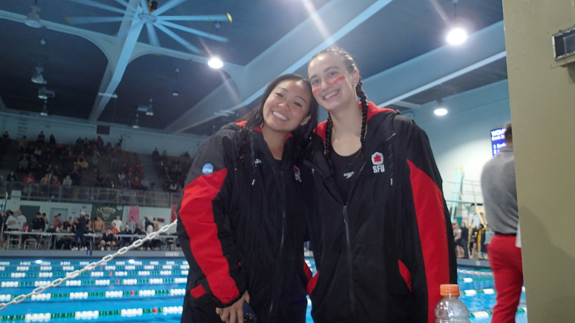 Two athletes from SFU Women's Swimming smile in front of the pool at the Logger Invitational in Washington