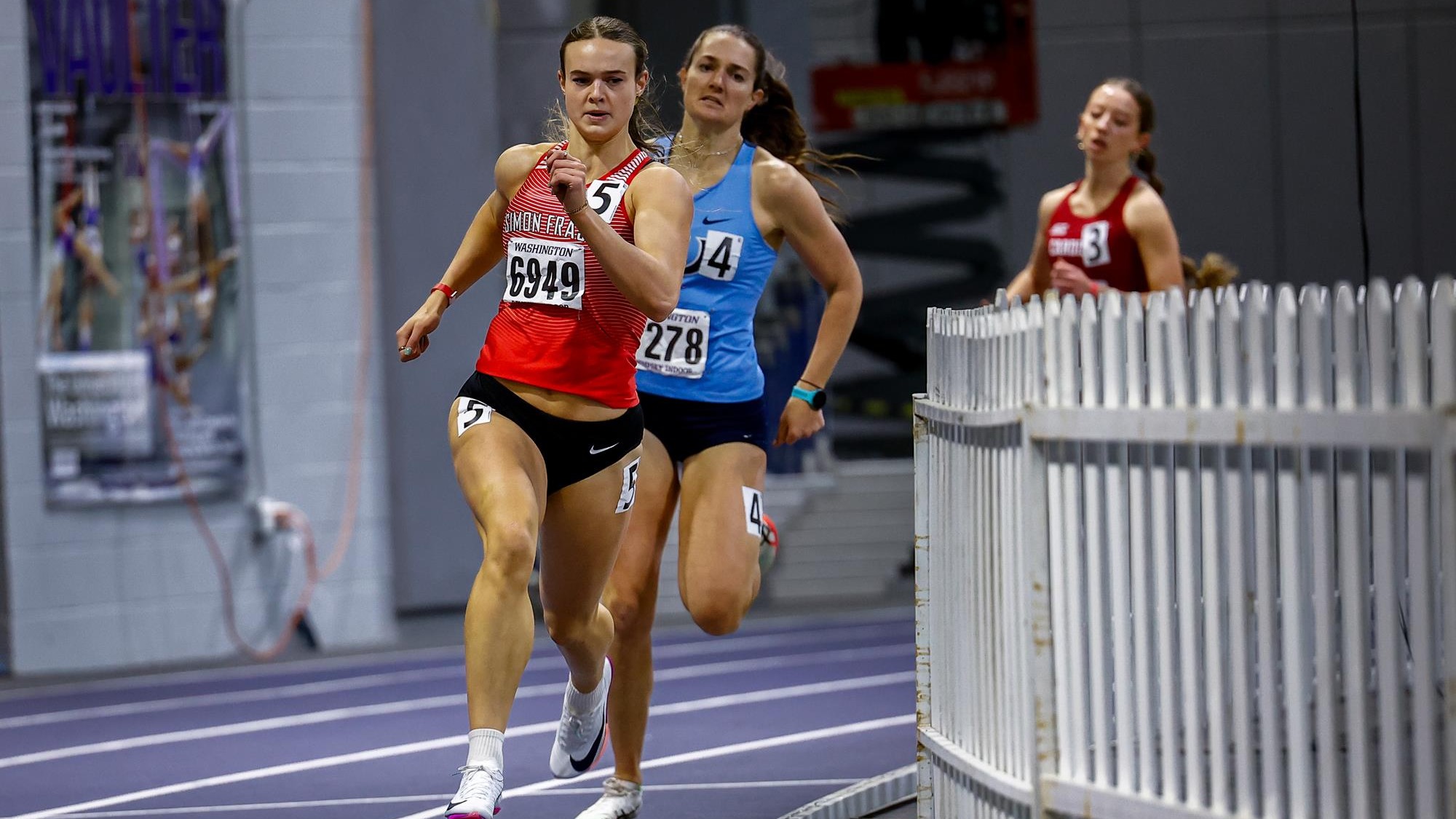 Emma Cannan running around the indoor track ahead of a competitor.