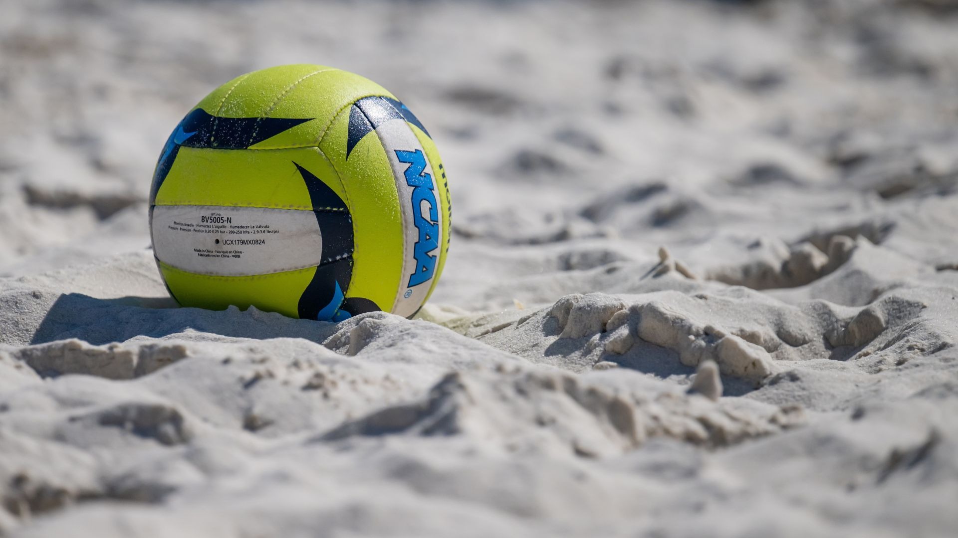 A blue and yellow volleyball rests on the sand.