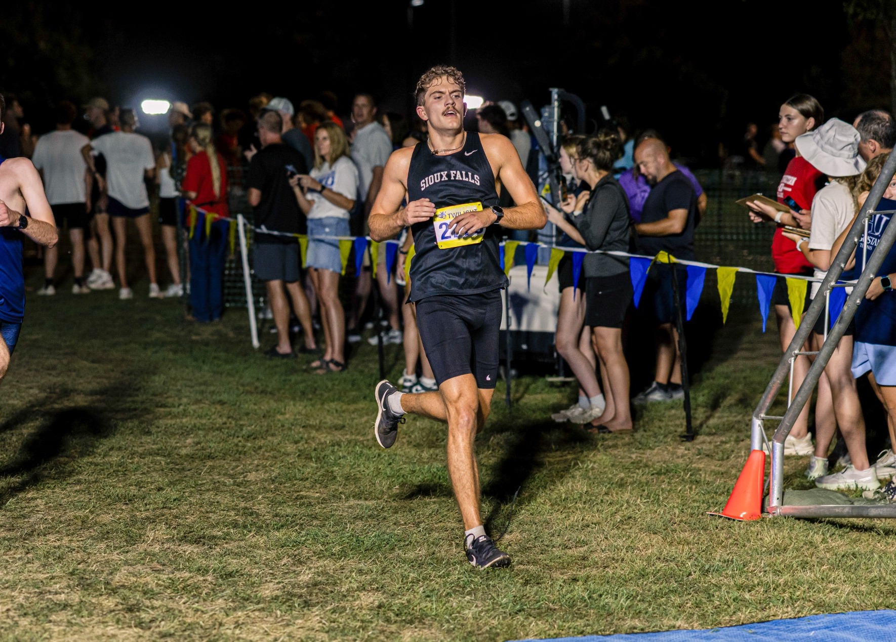 Men's cross country runner running during race in front of fans.