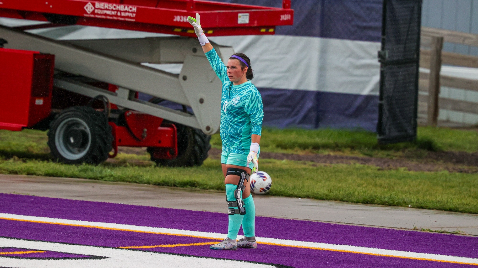 Women's soccer goalkeeper stands with hand in air while waiting to kick the ball