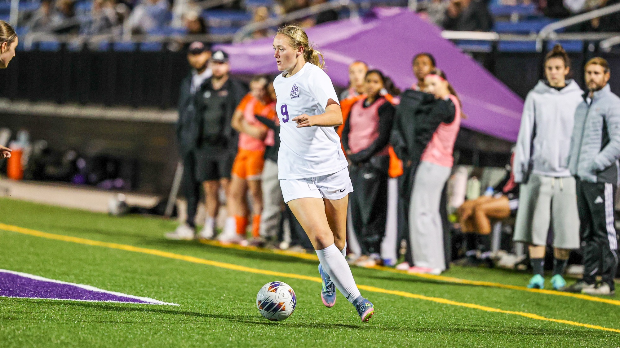Womens Soccer looking to pass ball while in front of opposing bench