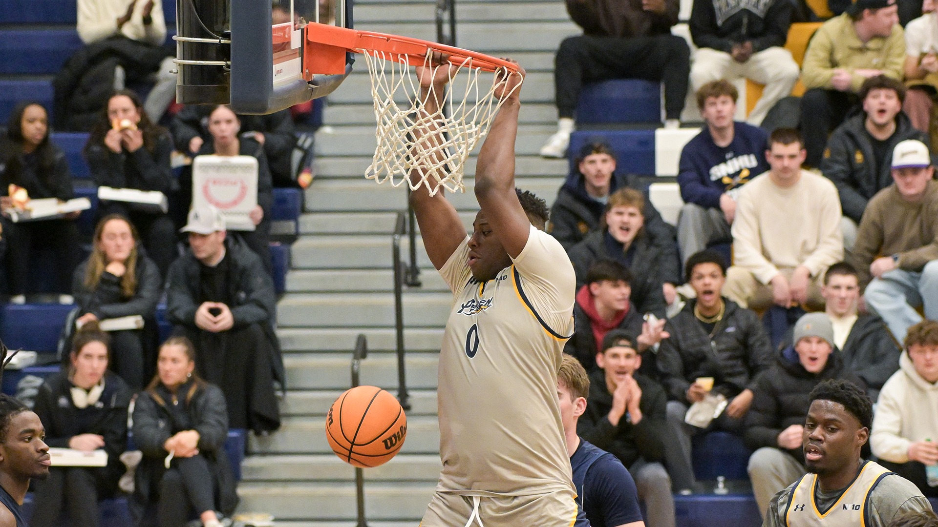 Ugo Nwachukwu hanging on the rim after dunking the basketball