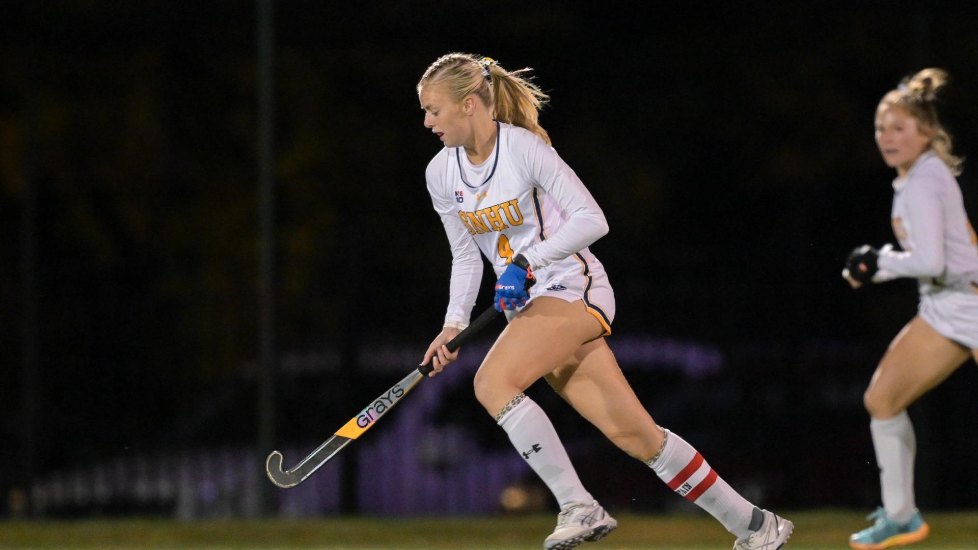 Field hockey player Amelia Crocombe pushes the ball with her stick as a teammate looks on