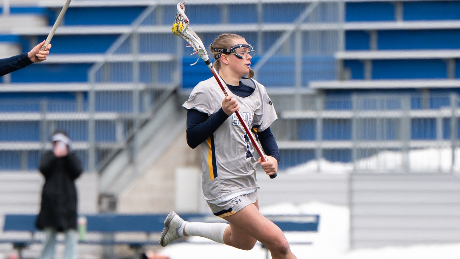 Piper Knowlton running with the ball in her stick and a defender trailing behind