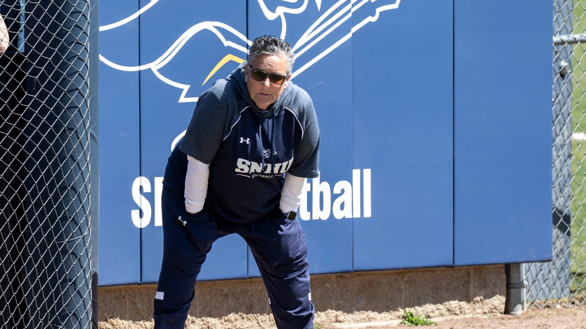 Head Coach Deb Robitaille of softball watches the action from the third base coaching box