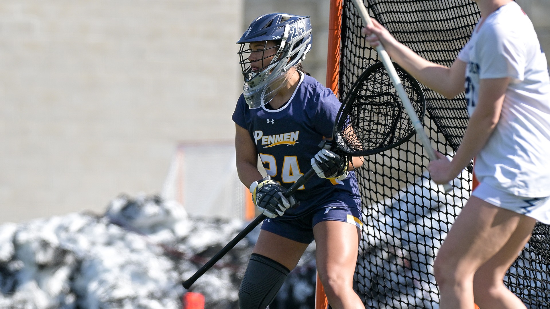 Corrina Moulton standing ready in the net with her stick, while an opponent stands to her left in the foreground