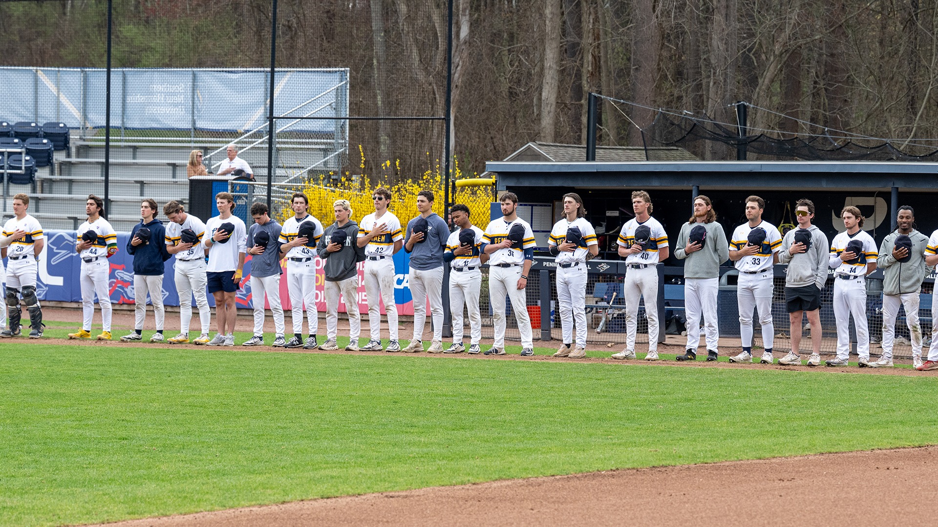 members of the SNHU baseball team lined up along the third base line during the National Anthem
